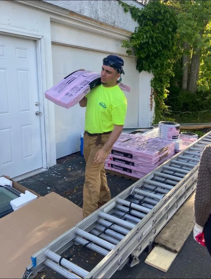 Sousa Roofing crew member carrying shingle bundles on a job site
